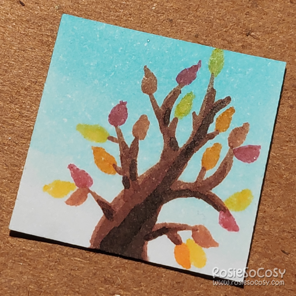 An inch sized illustration of a tree with branches and red, orange, yellow and some green leaves. The background is a blue sky.