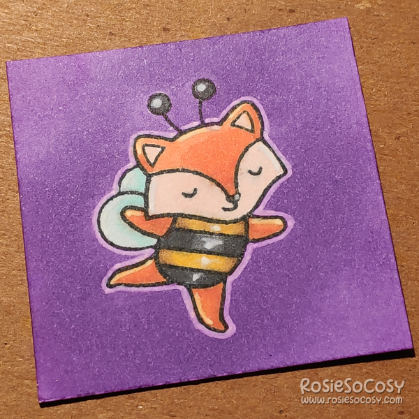 A tiny 2 inch card with an orange fox dressed up in a black and yellow bee costume. The fox is dancing with their eyes closed. The background is purple.