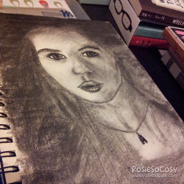 A charcoal drawing of Amy Pond (portrayed by Karen Gillan) in Doctor Who. Amy is looking at the camera. She has big eyes and somewhat pouted lips. She is wearing a necklace with the letter A on it.