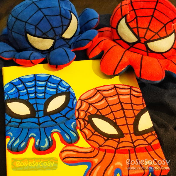 A canvas painting done in Posca markers, with two reversible octopus plushies on it. These are inspired by Spiderman. One is dark blue, the other is red. Both have a Spiderweb pattern all over.