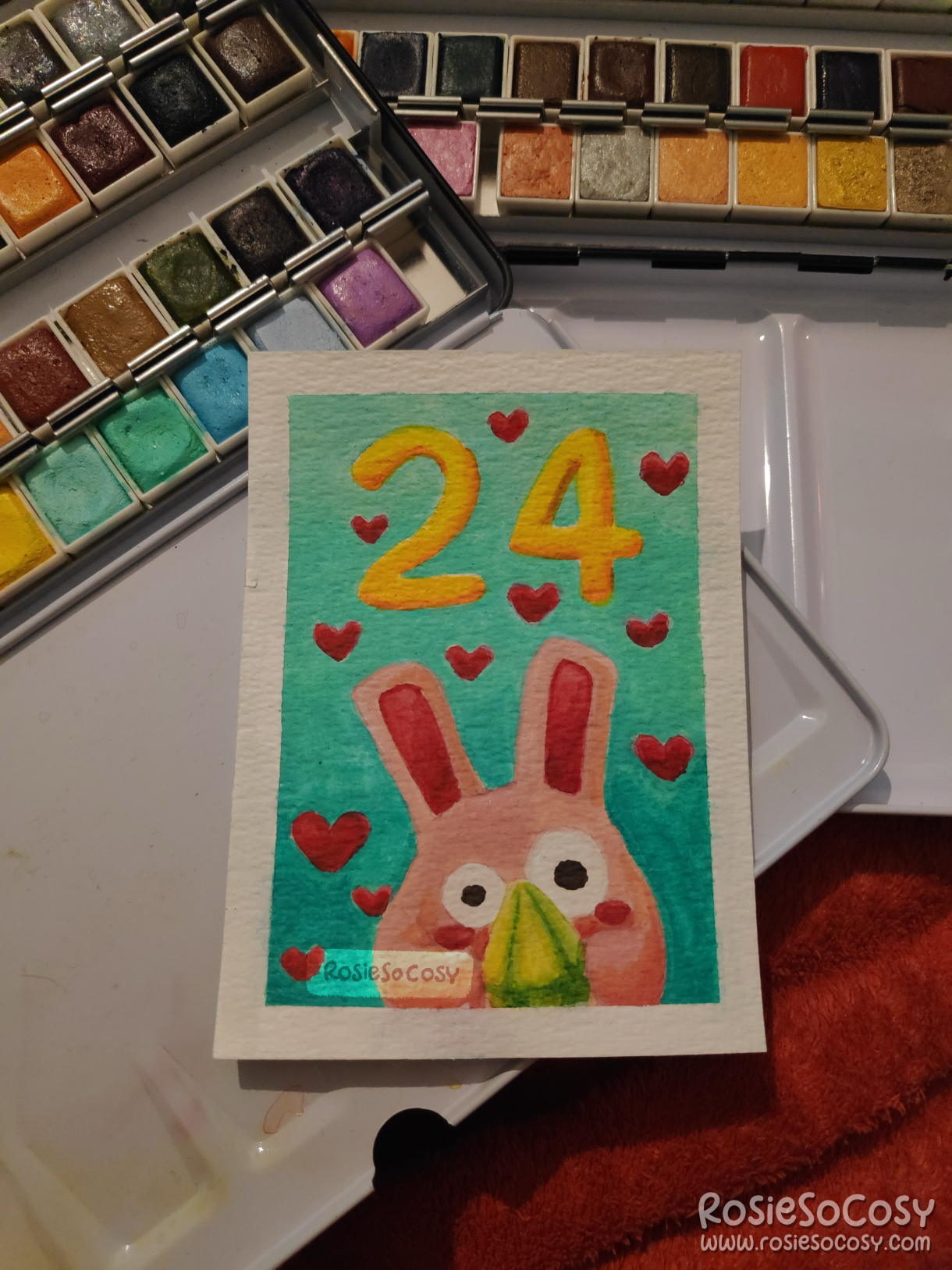 Watercolour illustration of a cute pink Freezer Bunny, holding a green plumbob, surrounded by red hearts, on a turquoise and teal gradient background, with the number 24 above it in yellow.