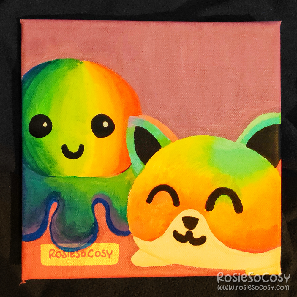 A canvas painting done in Posca markers, with two plushies on it. One is a rainbow octopus, the other a rainbow cat.