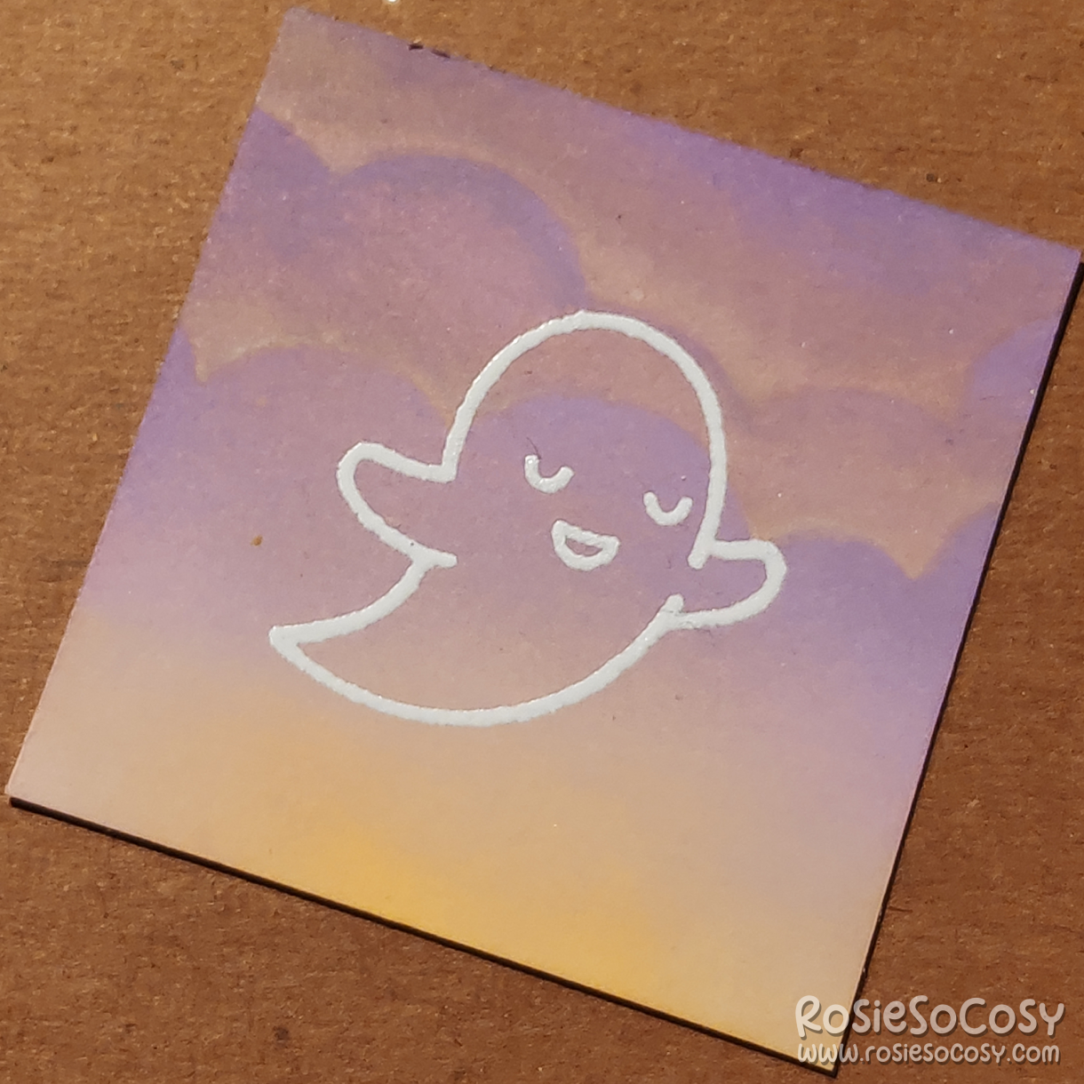 A tiny 2 inch card with a translucent (white outlined) ghost, who is seemingly peaceful, on a soft purple and yellow cloudy background.