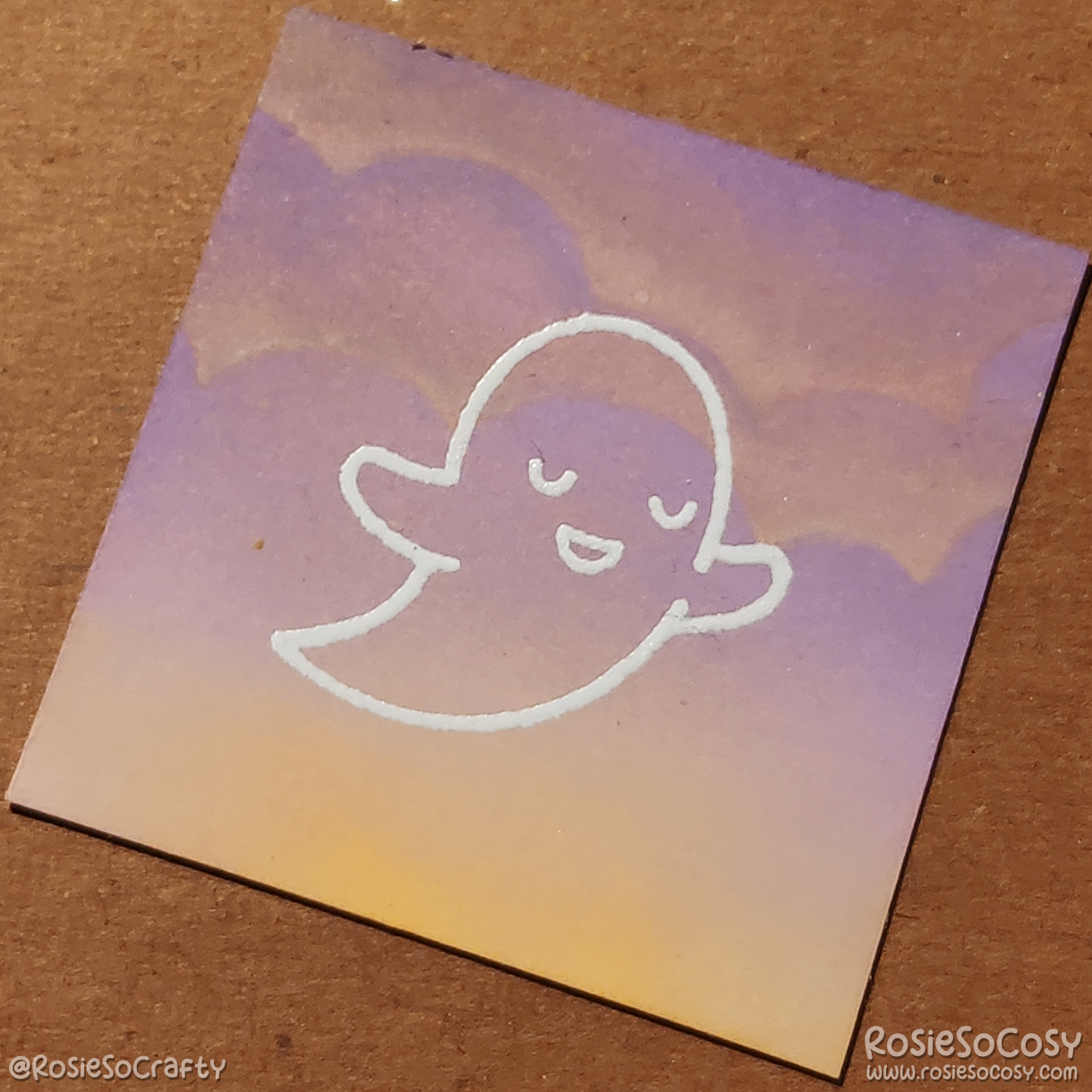 A tiny 2 inch card with a translucent (white outlined) ghost, who is seemingly peaceful, on a soft purple and yellow cloudy background.